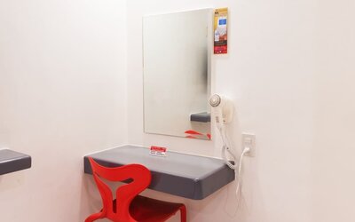 In-room workspace featuring a floating gray desk, rectangular wall mirror, bright red chair, wall-mounted hairdryer, and electrical outlet at Hotel Sogo Guadalupe.