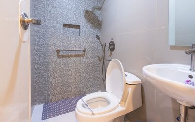 Accessible-style bathroom with a white toilet, handheld shower, wall-mounted grab bar, gray-and-white mosaic shower wall, and white pedestal sink at Hotel Sogo Guadalupe.