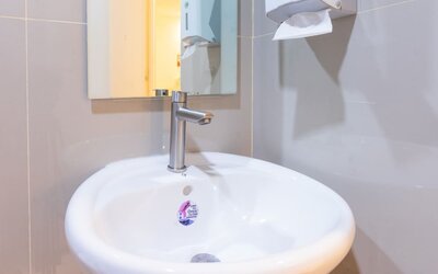 Close-up of a white round bathroom sink with a modern silver faucet, rectangular wall mirror, and wall-mounted soap and paper towel dispensers at Hotel Sogo Guadalupe.