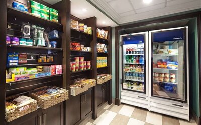 Hotel convenience shop stocked with snacks, candy, toiletries, over-the-counter essentials, refrigerated drinks, and frozen food items.