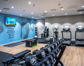 Modern hotel fitness center equipped with treadmills, an elliptical machine, exercise equipment, a dumbbell rack, workout bench, exercise ball, and wall-mounted television.