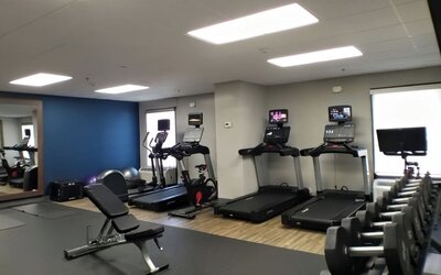 Hotel fitness center equipped with treadmills, elliptical machines, stationary bikes, a weight bench, dumbbells and exercise balls, with mirrors and large windows providing natural light.