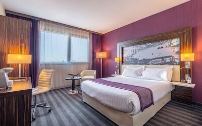 Guest room with a king bed, purple accent wall, airplane artwork, work desk, office chair, and bedside lamps at Holiday Inn Toulouse Airport.