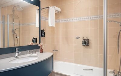 Bathroom with bathtub, glass shower screen, large mirror, vanity sink, toiletries, and towel rack at Holiday Inn Toulouse Airport.