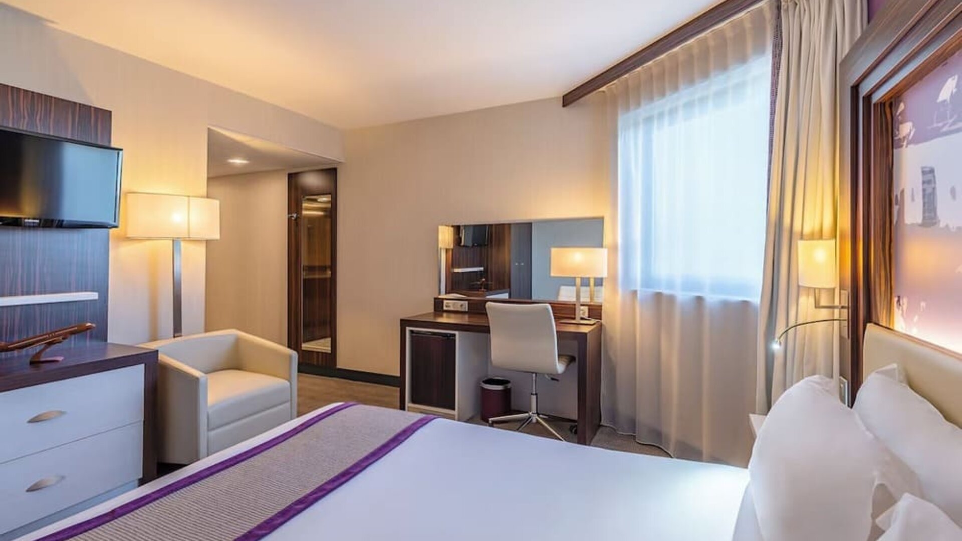 Guest room with a king bed, TV, armchair, work desk, bedside tables, and purple accent wall at Holiday Inn Toulouse Airport.