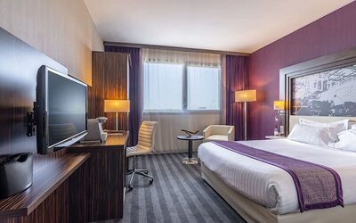 Guest room with a king bed, TV, work desk, armchair, wardrobe, and purple accent wall at Holiday Inn Toulouse Airport.