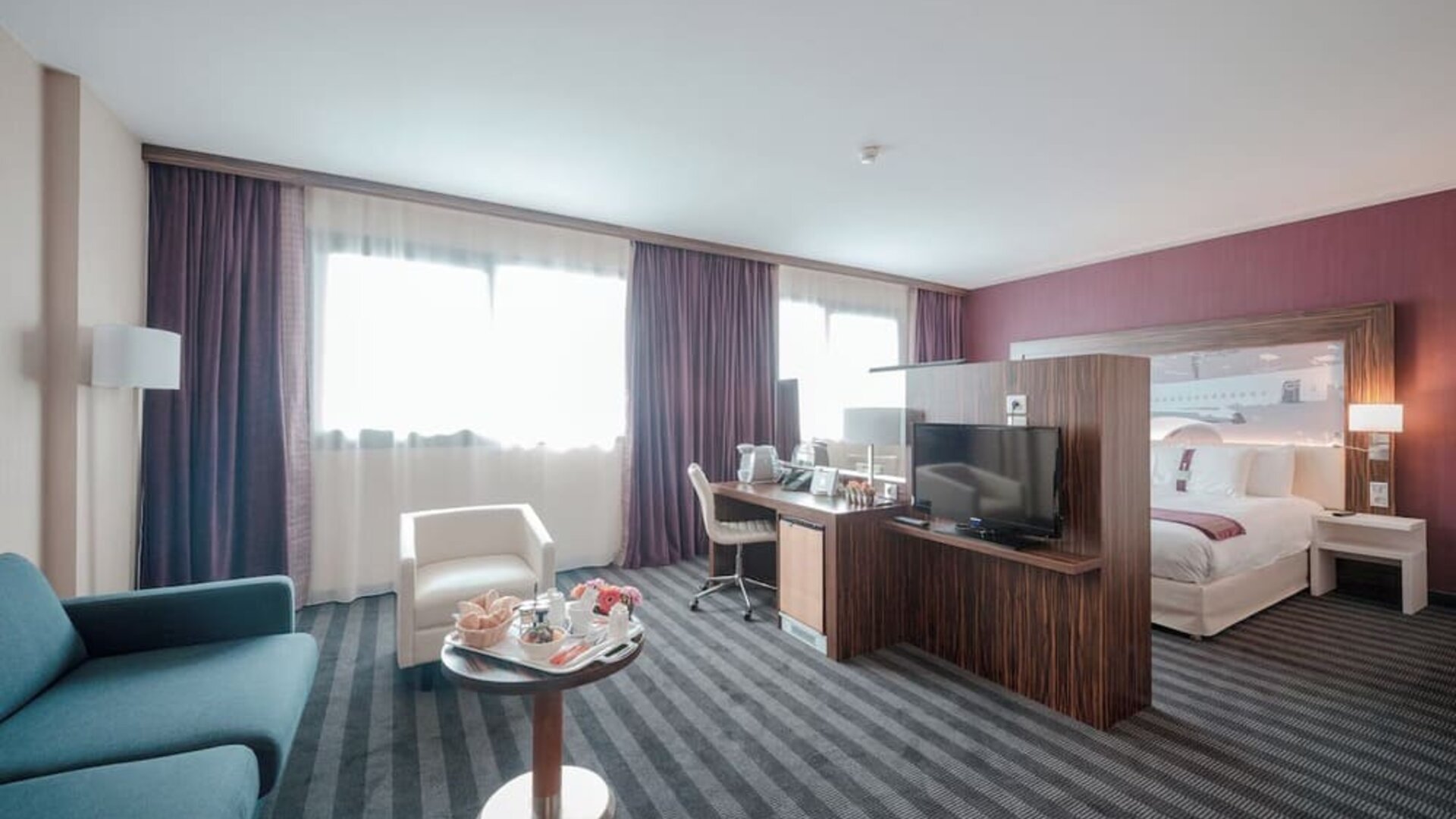 Spacious guest room with a king bed, separate seating area, sofa, coffee table, work desk, and large windows at Holiday Inn Toulouse Airport.