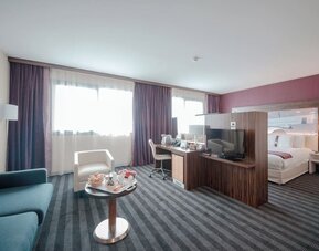 Spacious guest room with a king bed, separate seating area, sofa, coffee table, work desk, and large windows at Holiday Inn Toulouse Airport.