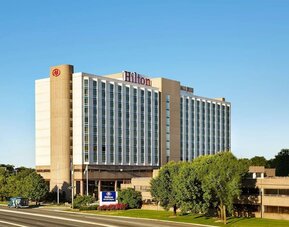 Exterior of Hilton Newark Airport with a multi-story facade, landscaped grounds, entrance driveway, and Hilton signage.