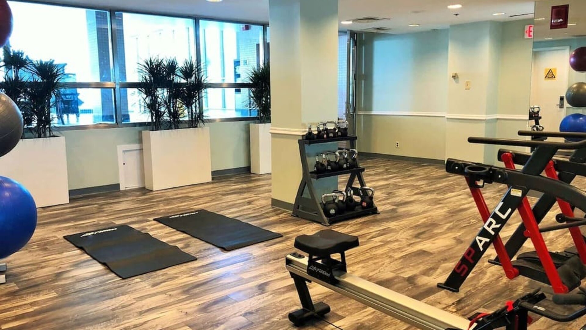 Hotel fitness center with exercise mats, dumbbells, resistance equipment, stationary bikes, rowing machine, and large windows at Hilton Newark Airport.