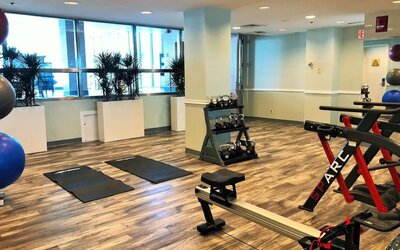 Hotel fitness center with exercise mats, dumbbells, resistance equipment, stationary bikes, rowing machine, and large windows at Hilton Newark Airport.