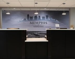 Reception desk at At Home Inn & Suites with a large Memphis, Tennessee cityscape mural behind the front desk.