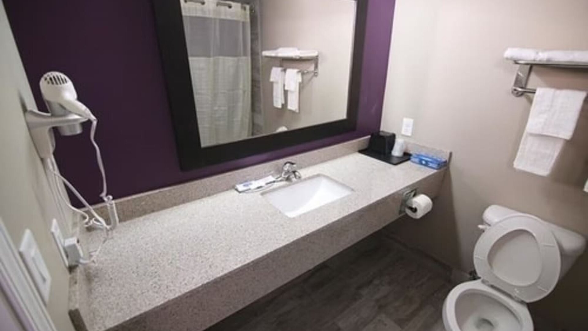 Bathroom with a granite vanity, sink, large mirror, hairdryer, towels, and toilet at At Home Inn & Suites.