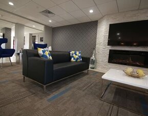 Hotel lounge with black sofas, blue armchairs, a fireplace, wall-mounted television, and white coffee tables at At Home Inn & Suites.