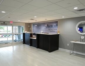 Hotel lobby with reception desks, entrance doors, decorative console table, and round wall mirror at At Home Inn & Suites.