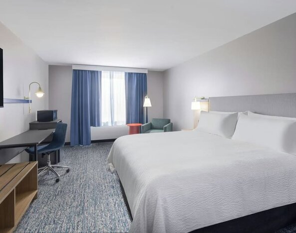 1. Spacious guest room with a king bed, white linens, desk and chair, television, seating area, blue curtains, and patterned carpet at Garner by IHG.