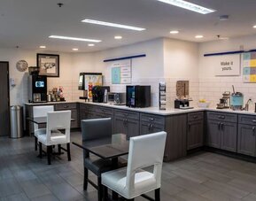 Hotel breakfast area with tables and chairs, beverage stations, food counters, and modern cabinetry at Garner by IHG.
