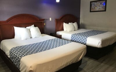Guest room with two beds featuring white linens, dark wood headboards, patterned blue bed runners, and a purple accent wall at Summit Inn Near Houston Medical Center-NRG Park.