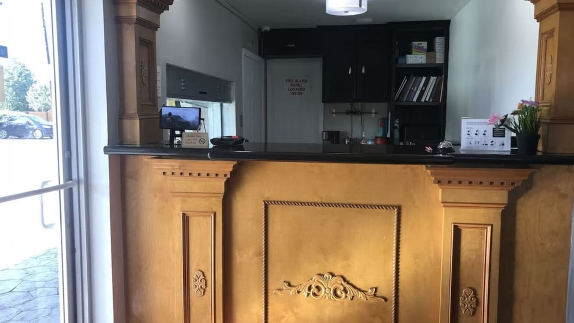 Hotel reception desk with an ornate wood-paneled counter, computer monitor, guest information, and decorative furnishings at Summit Inn Near Houston Medical Center-NRG Park.