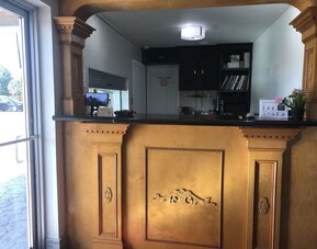 Hotel reception desk with an ornate wood-paneled counter, computer monitor, guest information, and decorative furnishings at Summit Inn Near Houston Medical Center-NRG Park.