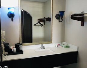 Bathroom vanity with a large framed mirror, white countertop, integrated sink, wall-mounted towel rack, and decorative blue wall sconces at Summit Inn Near Houston Medical Center-NRG Park.
