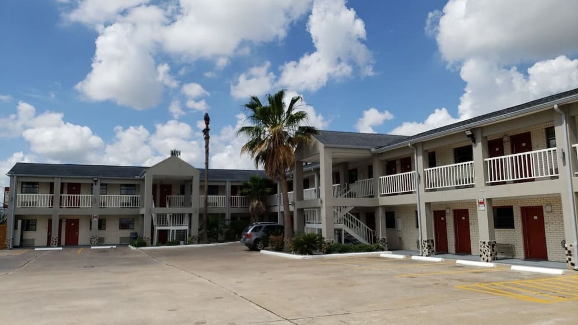 Exterior of Summit Inn Near Houston Medical Center-NRG Park showing the two-story hotel building, exterior corridors, red doors, parking area, and palm trees.