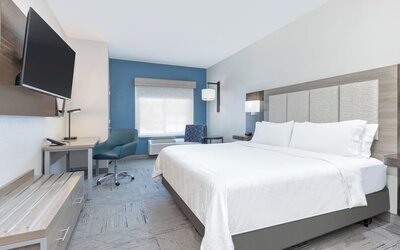 King guest room with a large bed, white bedding, blue accent wall, desk, armchair, and wall-mounted TV at Holiday Inn Express & Suites Granbury.