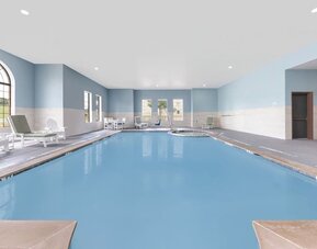 Indoor swimming pool with blue water, lounge chairs, large windows, and a separate whirlpool area at Holiday Inn Express & Suites Granbury.