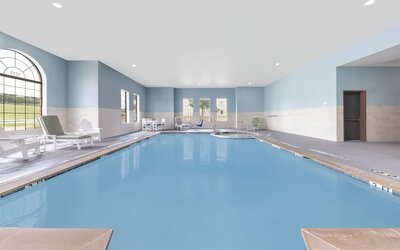 Indoor swimming pool with blue water, lounge chairs, large windows, and a separate whirlpool area at Holiday Inn Express & Suites Granbury.
