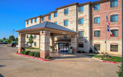 Front exterior of Holiday Inn Express & Suites Granbury showing the covered porte-cochère, landscaped grounds, parking area, and American and Texas flags.