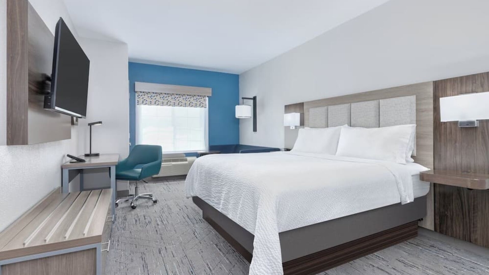 Bright guest room with a blue accent wall, large window, blue sofa, and king bed at Holiday Inn Express & Suites Granbury.
