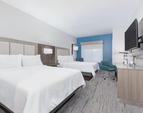 Guest room with two queen beds, white bedding, a wood-paneled headboard, blue accent wall, desk, armchair, and wall-mounted TV at Holiday Inn Express & Suites Granbury.