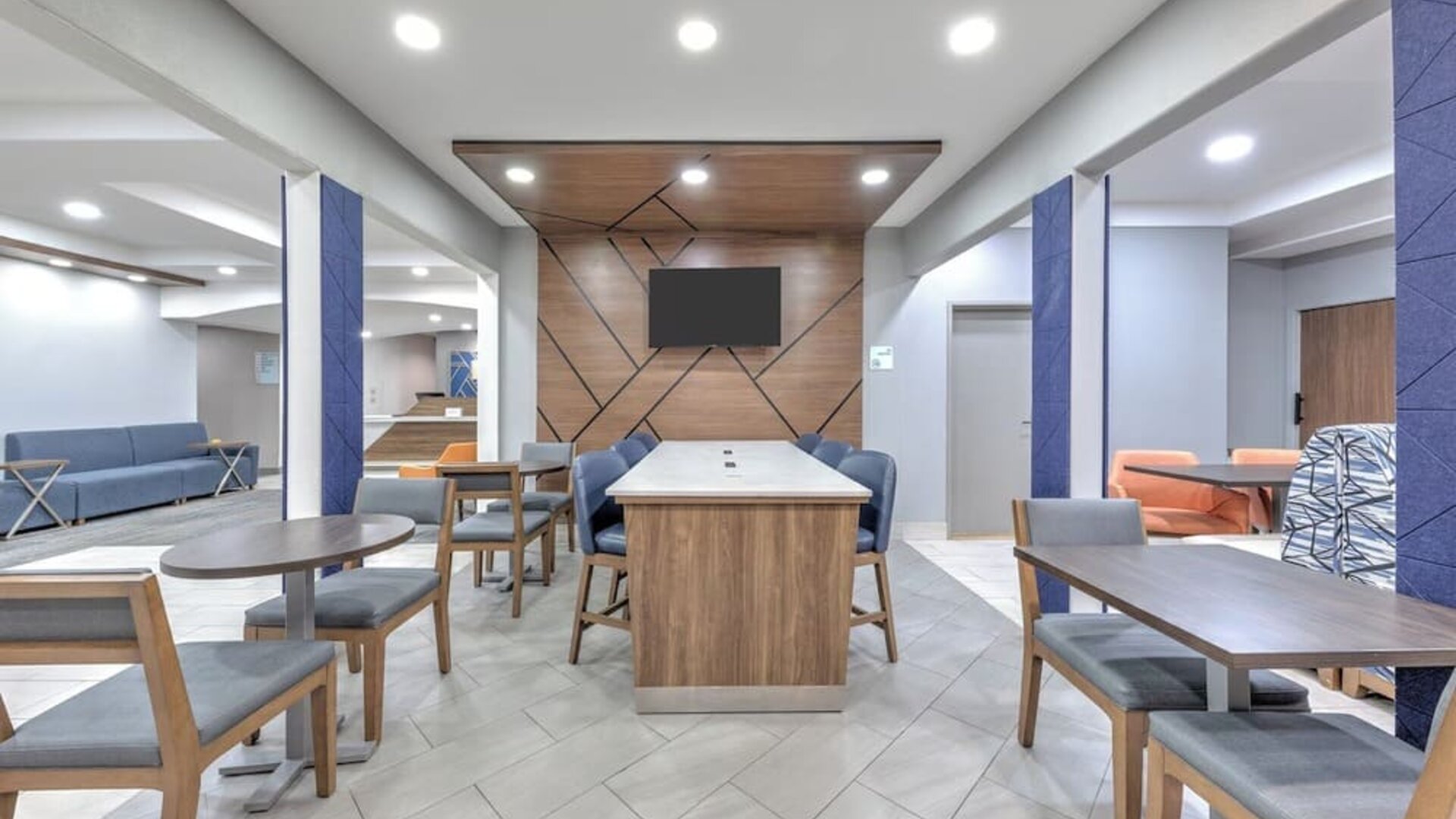 Hotel lobby with modern seating, tables, blue accent columns, wood paneling, and a wall-mounted TV at Holiday Inn Express & Suites Granbury.