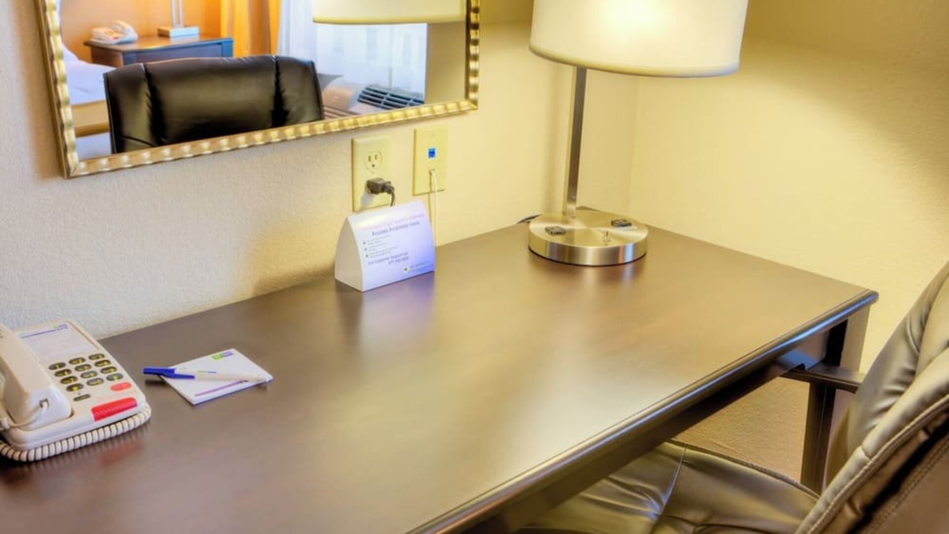 In-room workspace featuring a wooden desk, office chair, lamp, telephone, and wall mirror at Holiday Inn Express & Suites Granbury.