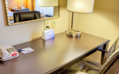 In-room workspace featuring a wooden desk, office chair, lamp, telephone, and wall mirror at Holiday Inn Express & Suites Granbury.