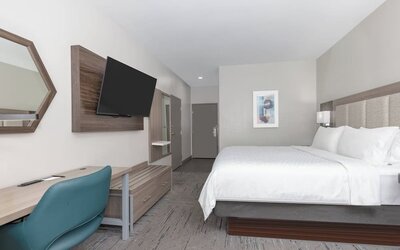 Spacious king guest room with a large bed, white bedding, wood furnishings, desk, blue office chair, and wall-mounted TV at Holiday Inn Express & Suites Granbury.