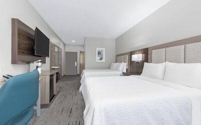 Guest room with two queen beds, white bedding, wood headboard, blue office chair, desk, dresser, and wall-mounted TV at Holiday Inn Express & Suites Granbury.