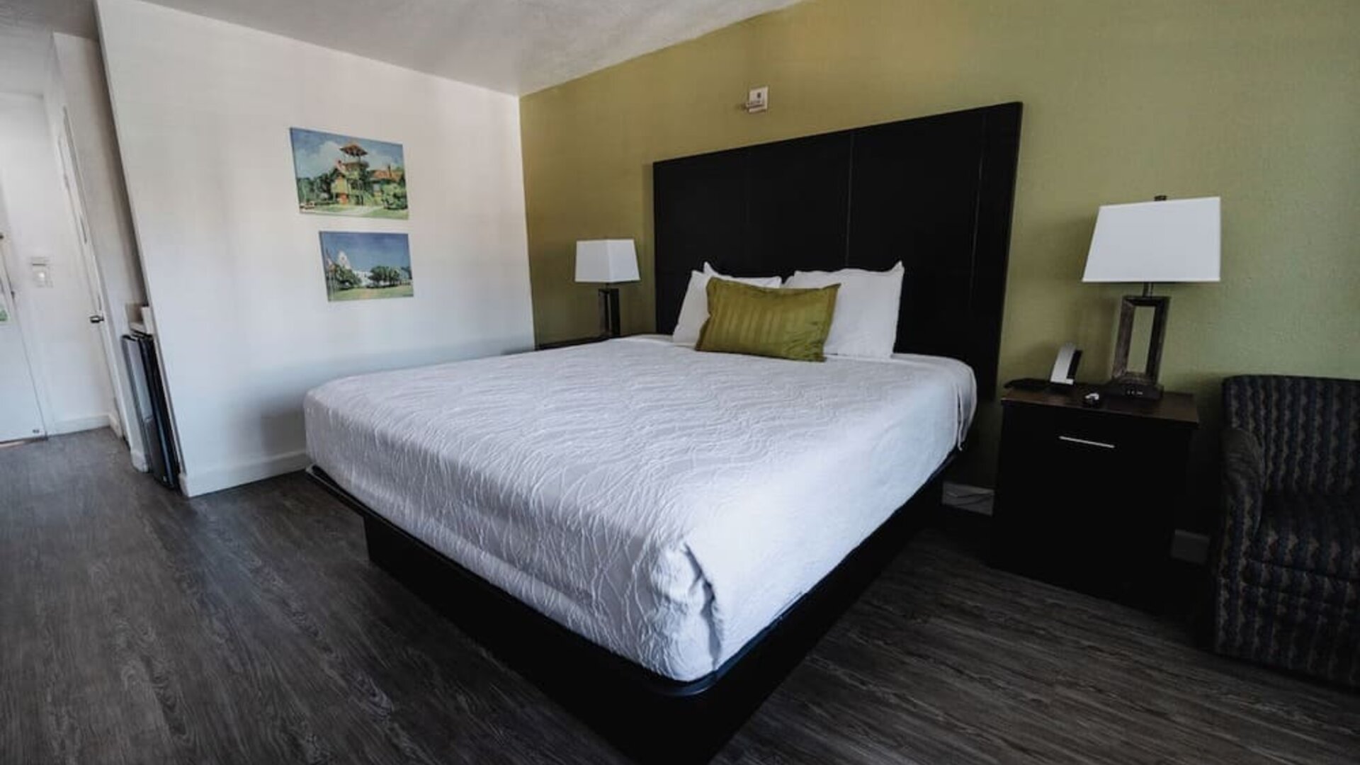 King guest room with white bedding, dark wood furnishings, green accent wall, bedside lamps, and a cushioned armchair at Western Inn.
