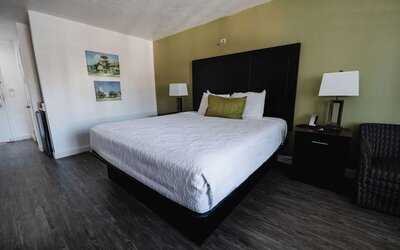 King guest room with white bedding, dark wood furnishings, green accent wall, bedside lamps, and a cushioned armchair at Western Inn.