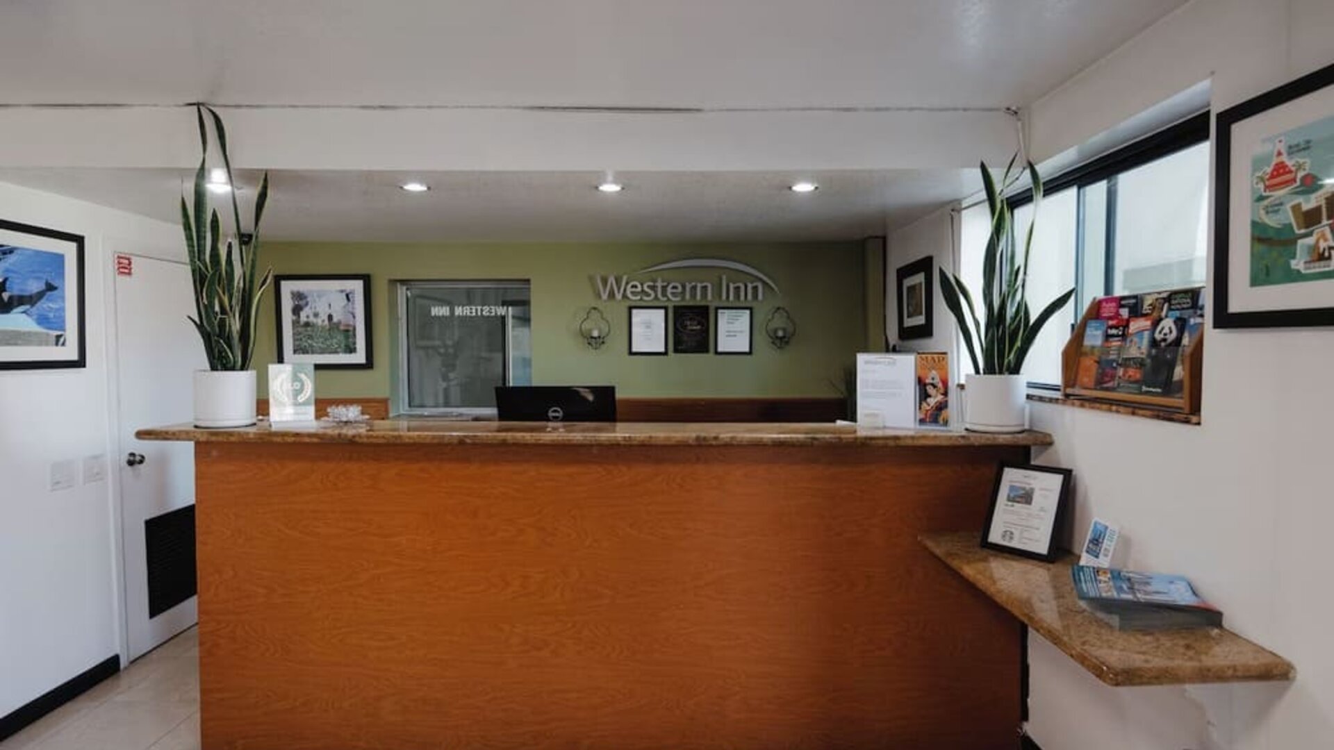 Reception desk with wooden counter, Western Inn signage, decorative plants, framed artwork, and guest information materials at Western Inn.