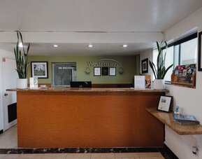 Reception desk with wooden counter, Western Inn signage, decorative plants, framed artwork, and guest information materials at Western Inn.