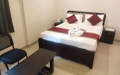 Comfortable double bed guest room featuring white linens, burgundy decorative pillows, matching bed runner, folded towels, bedside cabinets, and a seating area.