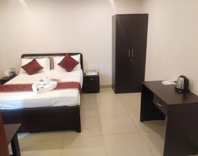Bright double bed guest room featuring white bedding, burgundy accents, a wooden wardrobe, bedside cabinets, and a refreshment station with an electric kettle.