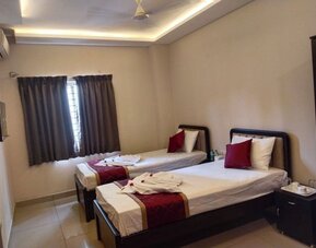 Comfortable twin bed guest room featuring white linens, burgundy decorative runners, matching pillows, folded towels, air conditioning, and a curtained window.