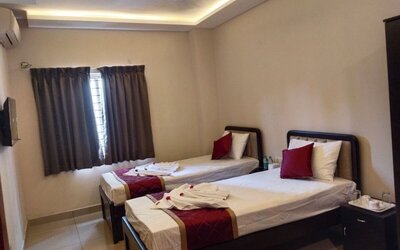 Comfortable twin bed guest room featuring white linens, burgundy decorative runners, matching pillows, folded towels, air conditioning, and a curtained window.