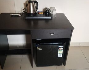 Black wooden refreshment station at The Nisarga Suites featuring an electric kettle, mugs, drinking glasses, beverage supplies, and a mini refrigerator.