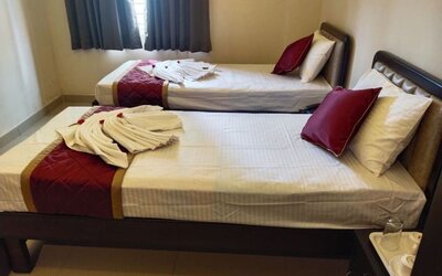 Neatly furnished twin bed guest room featuring white linens, burgundy quilted runners, decorative towel arrangements, dark wooden bed frames, and a curtained window.