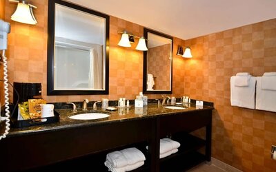 Bathroom with a double vanity, granite countertops, two sinks, large mirrors, warm-toned tiled walls, and neatly arranged towels at Best Western Plus BWI Airport Arundel Mills.