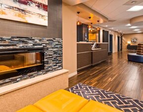 Hotel reception area with a front desk, modern wood finishes, decorative pendant lighting, patterned wall accents, and guest seating at Best Western Plus BWI Airport Arundel Mills.