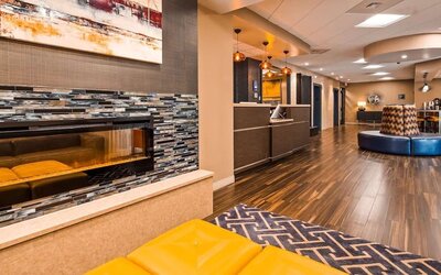 Hotel reception area with a front desk, modern wood finishes, decorative pendant lighting, patterned wall accents, and guest seating at Best Western Plus BWI Airport Arundel Mills.